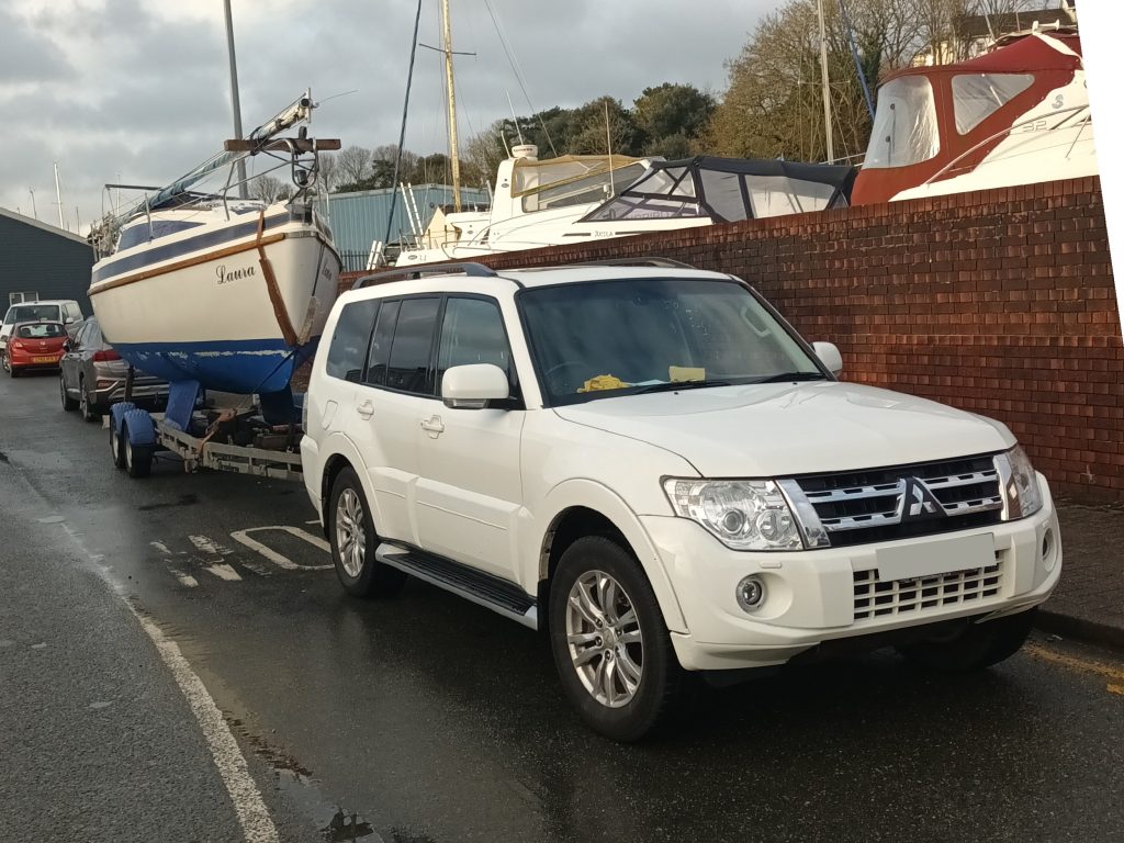 a white four wheel drive SUV with a sailing boat on a trailer